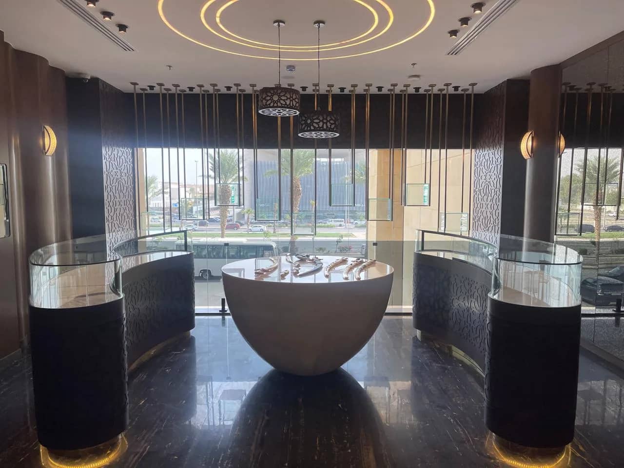 Display gallery with a bowl-shaped central table, curved glass showcases on CNC-cut bases and an LED ring ceiling