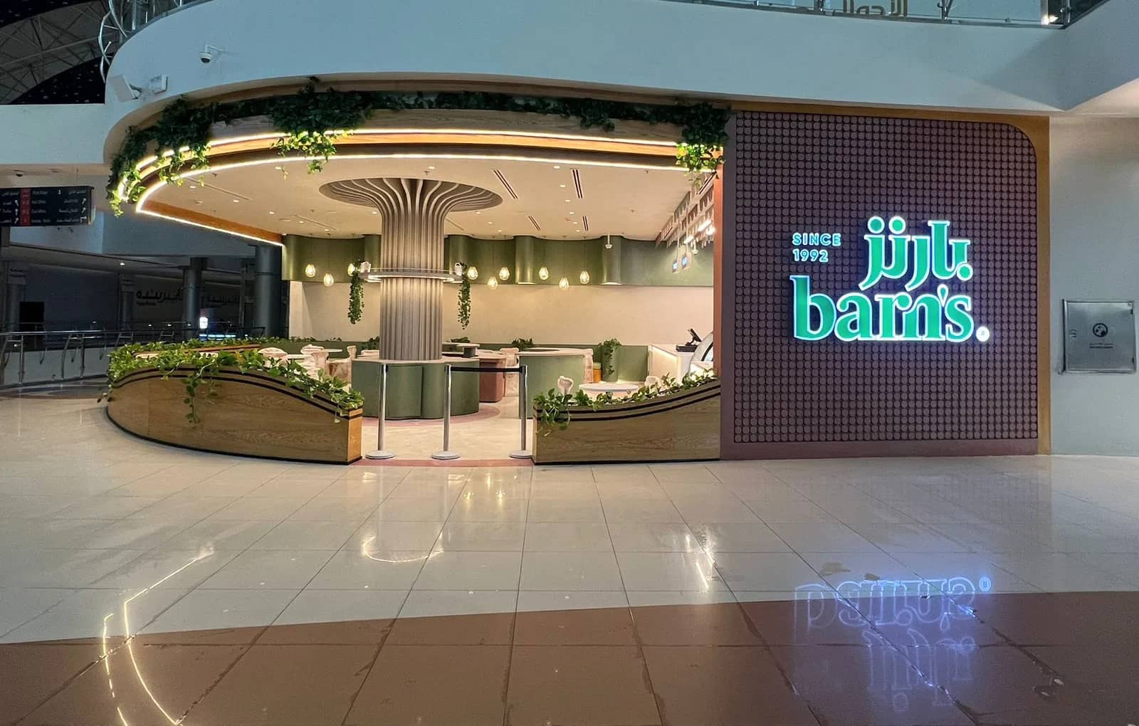 Barn’s coffee kiosk at Al Andalus Mall with an illuminated sign, a tree-shaped fluted column and timber planters